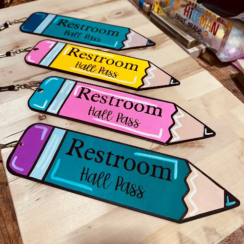Colorful pencil-shaped 'Restroom Hall Pass' tags on a wooden surface.