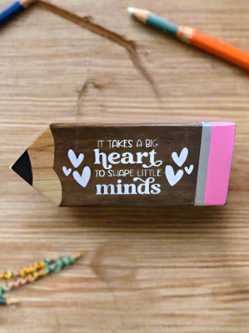 Wooden pencil-shaped block with 'It takes a big heart to shape little minds' text on a wooden surface.