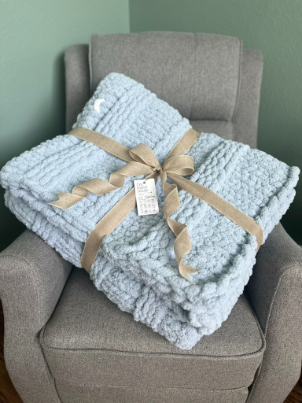 Light blue textured blanket with a beige ribbon on a gray armchair against a green wall.
