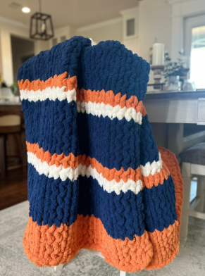 Knitted blanket with blue, orange, and white stripes on a chair in a room.