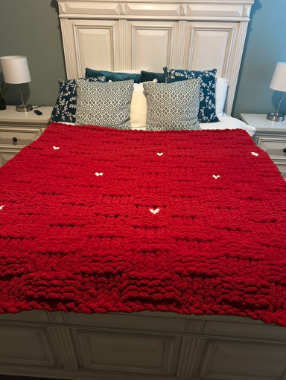 Red blanket with heart patterns on a bed in a bedroom setting.