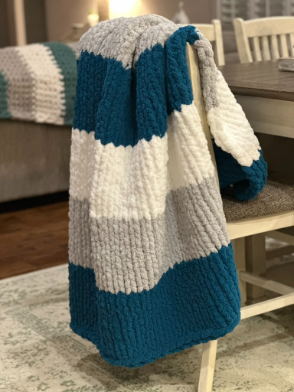 Knitted blanket with blue, gray, and white stripes draped over a chair in a room.