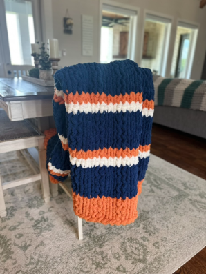 Knitted blanket with blue, orange, and white stripes draped over a chair in a room.