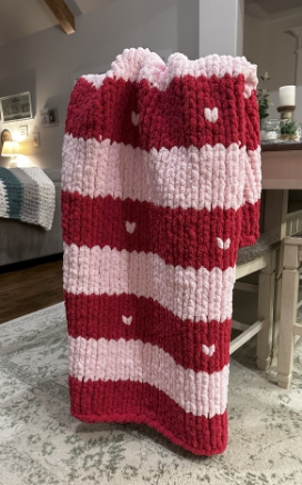 Red and pink striped knitted blanket with heart patterns in a living room. 