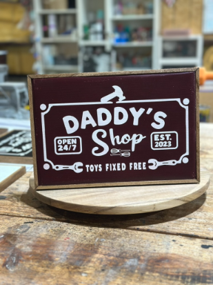 Wooden sign with 'Daddy's Shop' text on a wooden surface