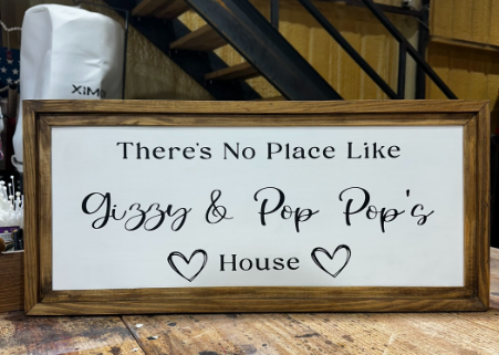 Wooden framed sign with text 'There's No Place Like Gizzy & Pop Pop's House' on a wooden floor.